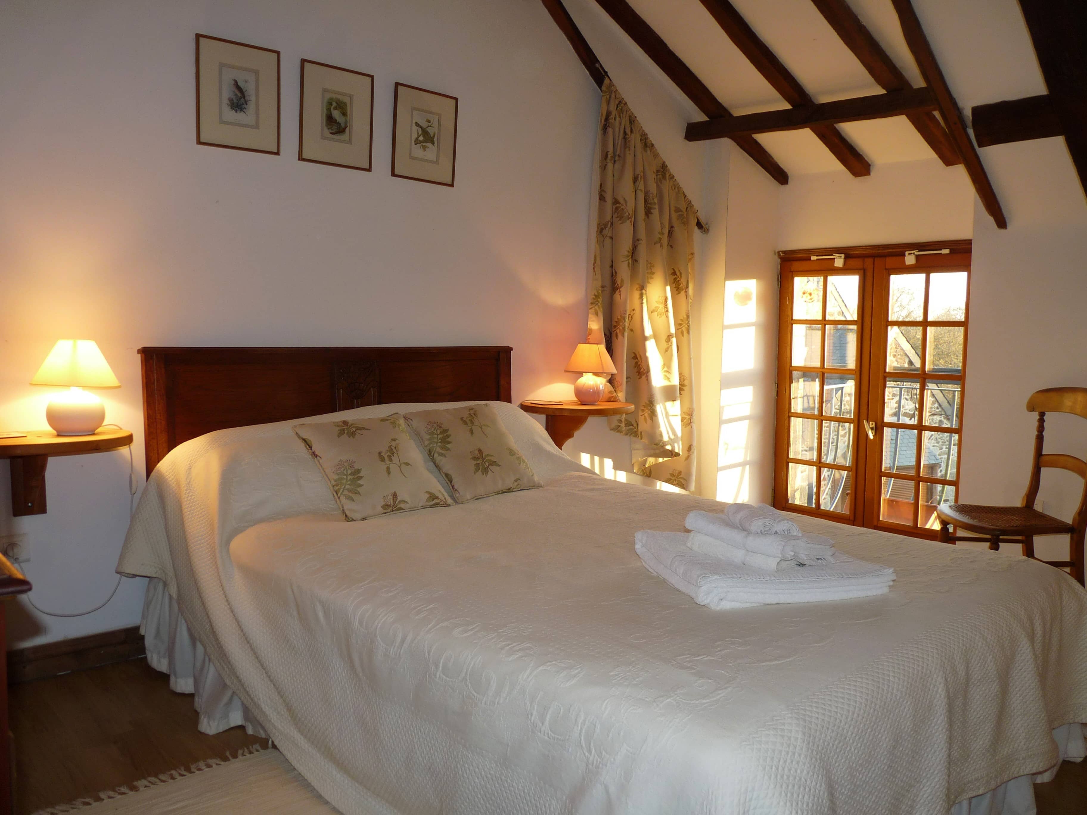 Spacious and comfortable bedroom of La Julerie cottage in Brittany, France, with a king-size bed, elegant rustic decor, a stone fireplace, and a panoramic view of the surrounding countryside. Perfect for a peaceful night's sleep after a day of sightseeing in the Brittany region.